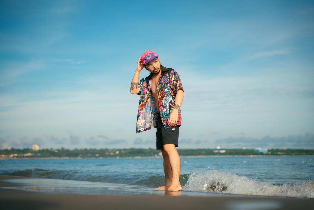 A man wearing a Hawaiian shirt stands on the beach.