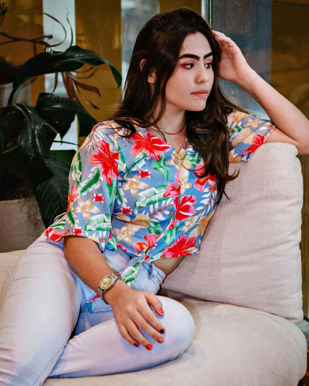A woman wearing a Hawaiian shirt is leaning against a sofa.